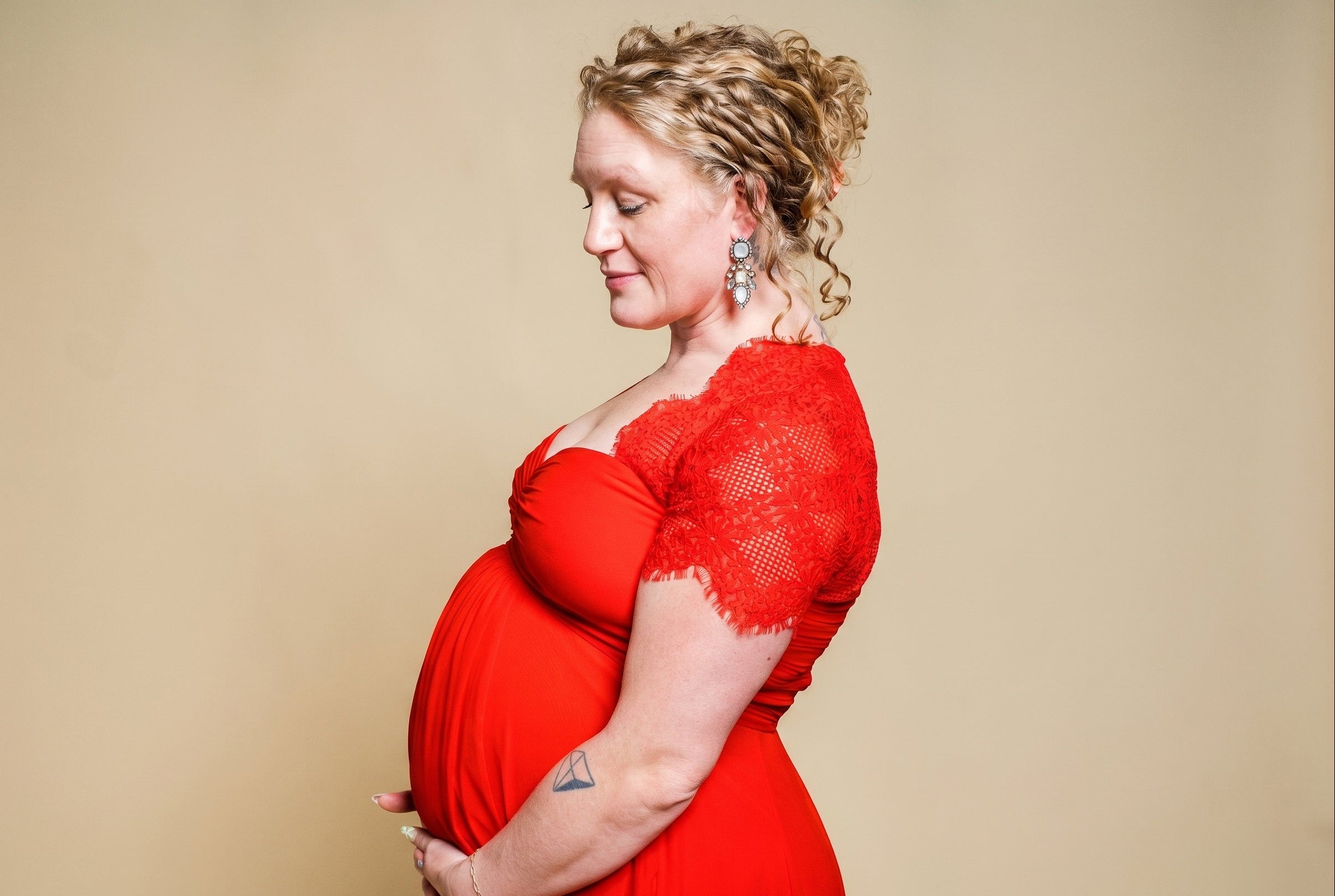 Pregnant woman in a red lace dress against a beige background